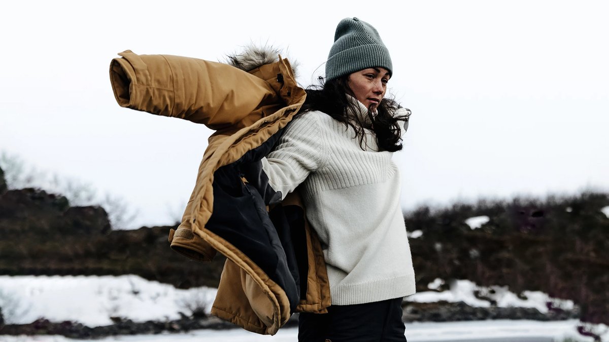 A woman puts on the Fjallraven Nuuk parka against a snowy background.