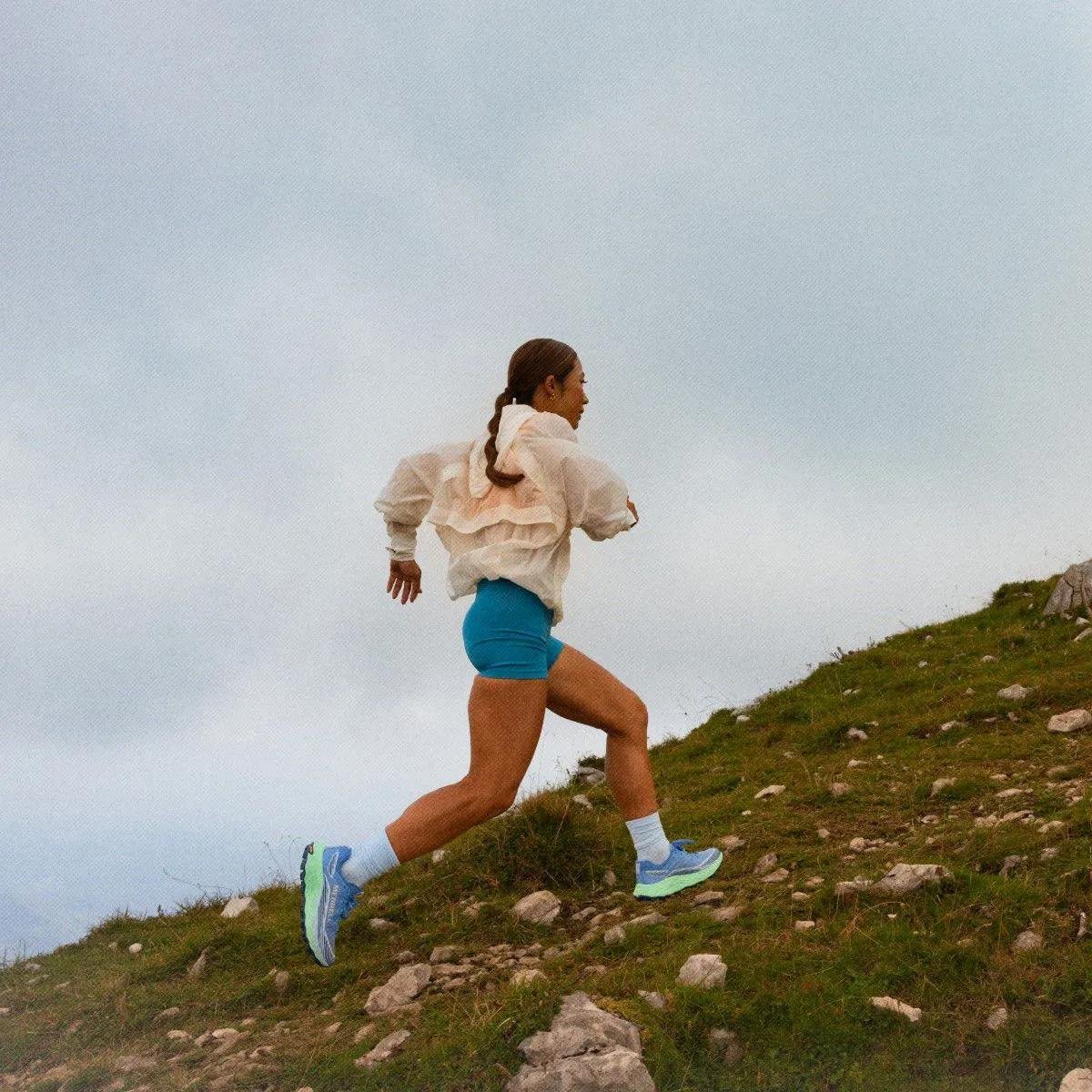Runner sprinting up a rocky hill in profile with the sky behind them.