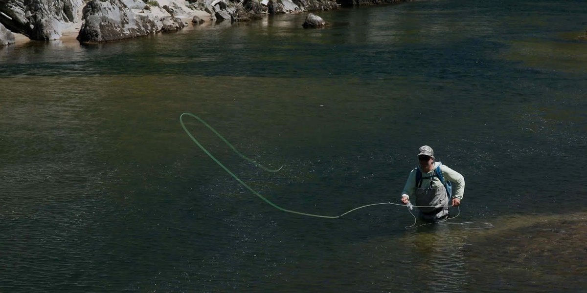 Fly fisherman in wading boots standing in a greenriver casting his line out.
