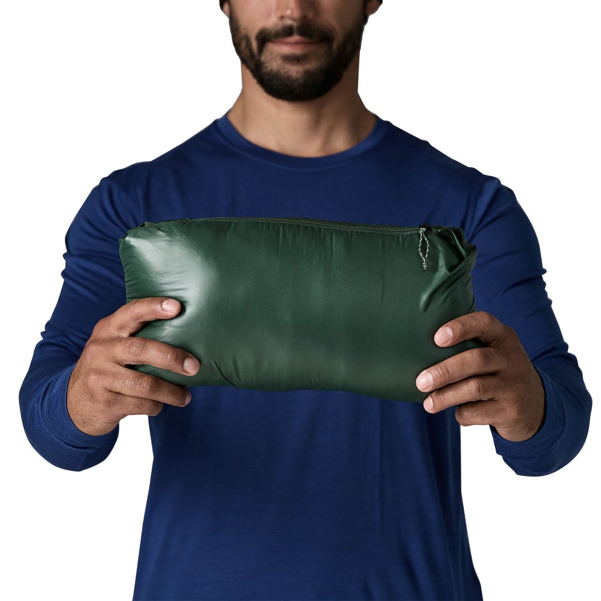 person standing holding durable down jacket that has been stuffed into itself into a compact oblong shape.