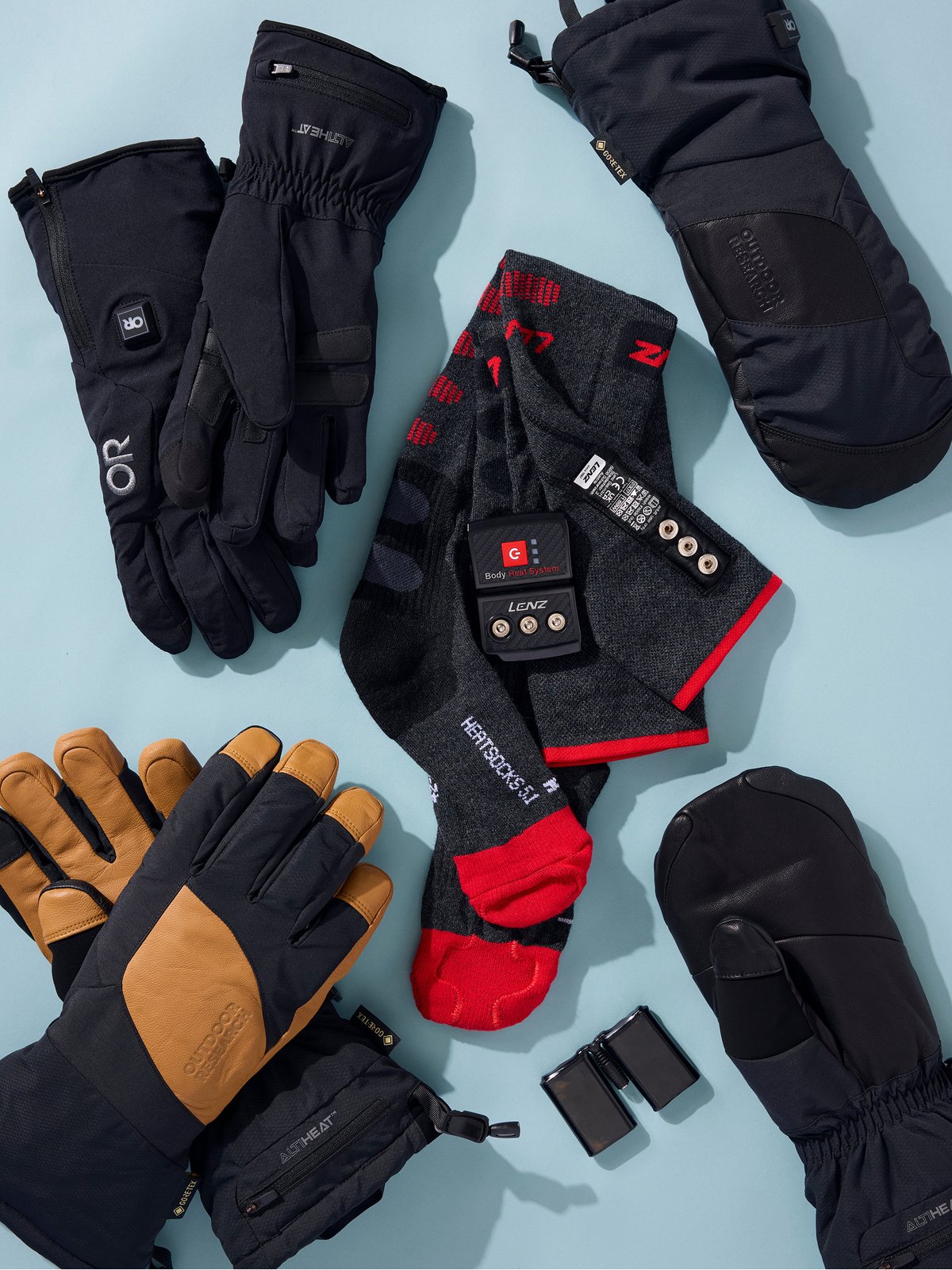 Heated gloves and heated ski socks with their batteries on a light blue background.