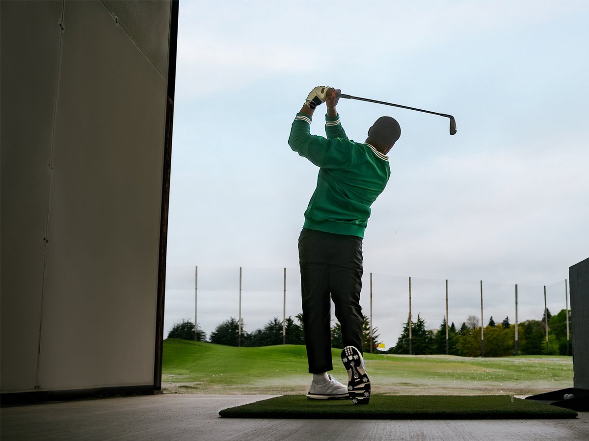 A man stands on a driving range, mid-swing.