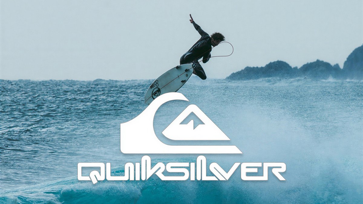 Professional surfer performing aerial maneuver on Quiksilver surfboard in blue ocean waves with coastal mountains in background.