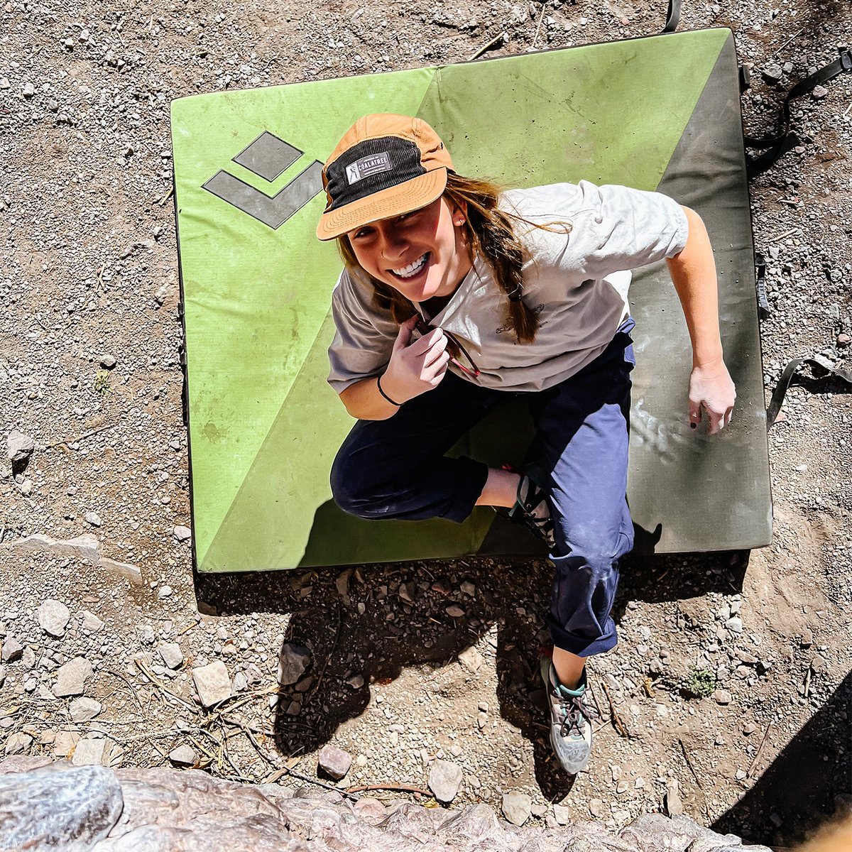 Climber sitting on crash pad smiling up from base of a bouldering problem while wearing Coalatree workwear hat.