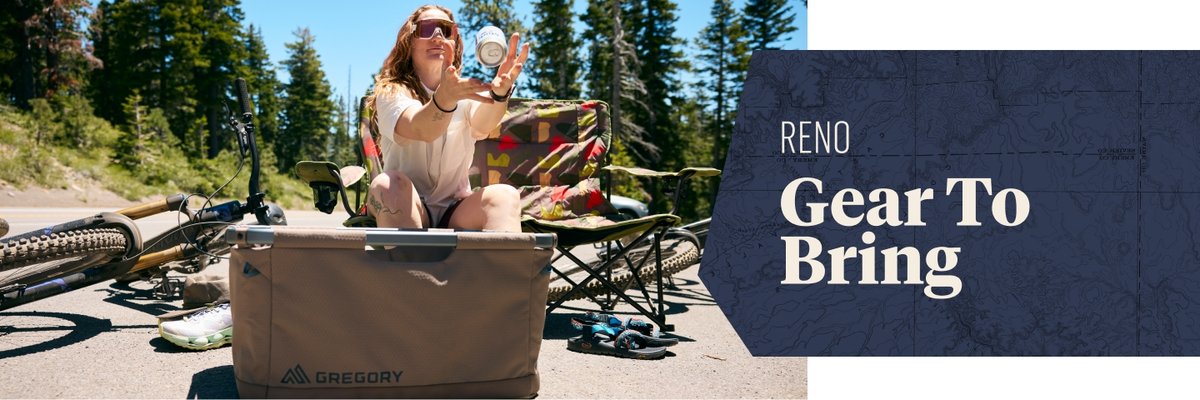 A woman with tattoos sits on a folding camp chair next to a mountain bike. Her arms are outstretched to catch a flying can of beer, a Modelo. Text to the right reads "RENO Gear To Bring" on a dark blue panel.