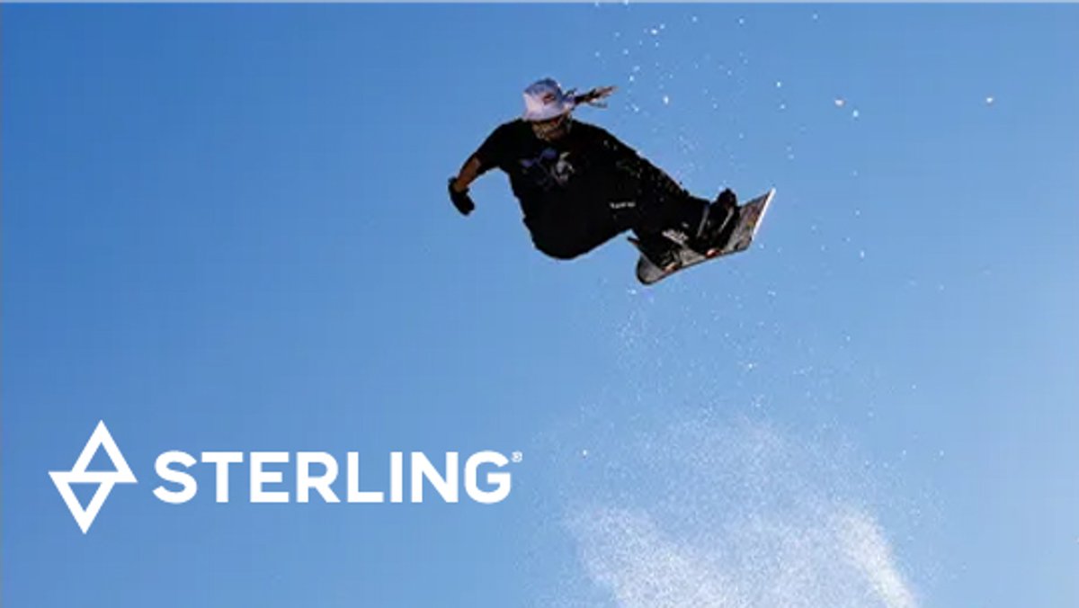 Professional snowboarder performing aerial trick against blue sky wearing Sterling branded gear and equipment.