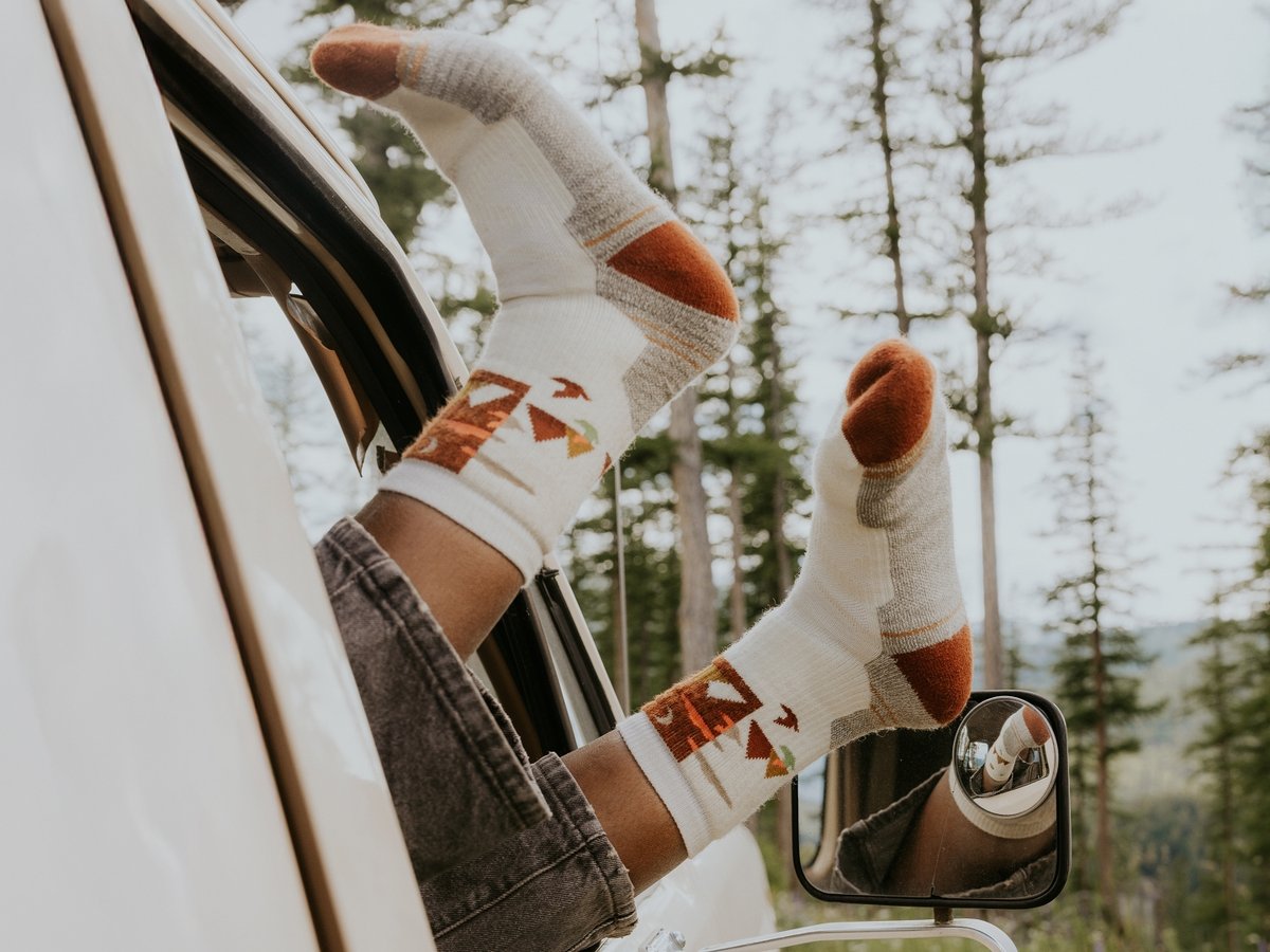 A person’s feet are hanging out an open car window. They are wearing colorful socks.