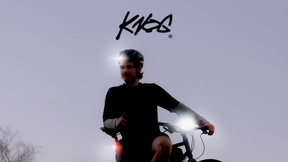 Man wearing black jacket and helmet riding bicycle at dusk with bright Knog LED front and rear lights for safety visibility.