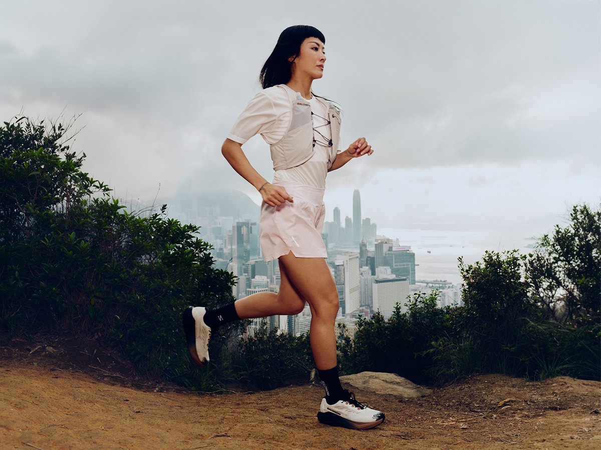 Runner on dirt trail lined with bushes with city skyline in the distance below.