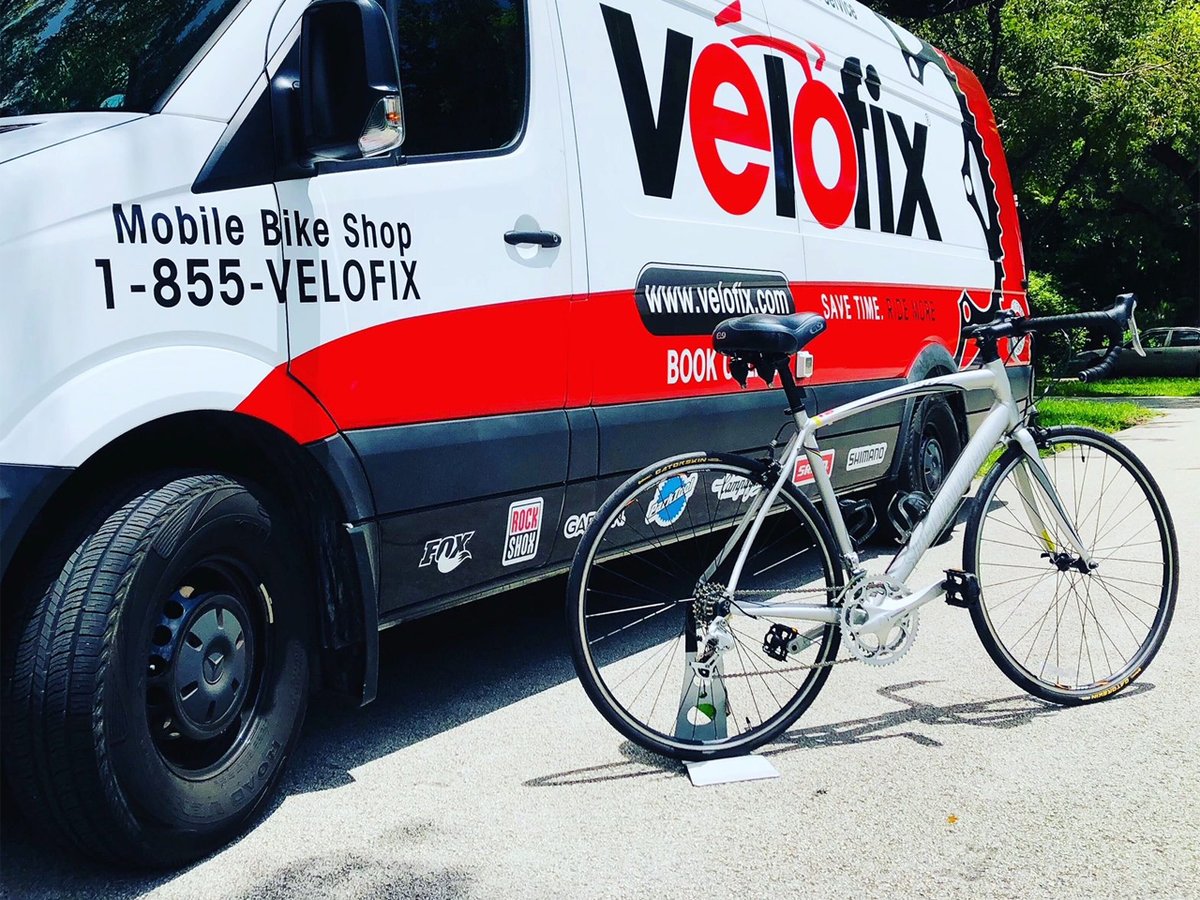 A road bike is on a stand outside a parked velofix van.