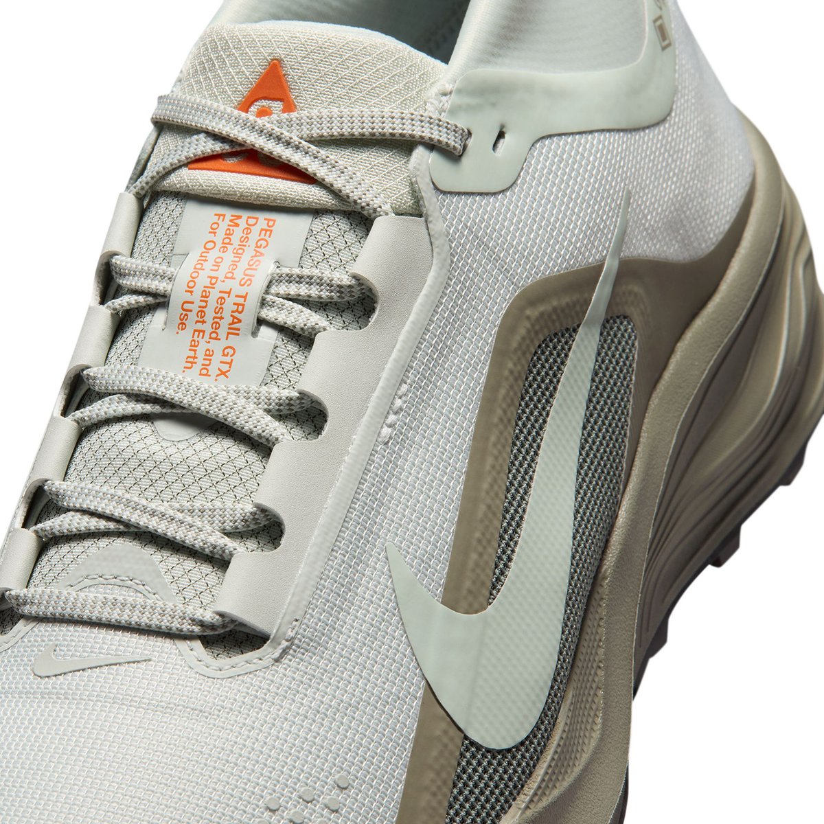 Close-up of the Nike ACG Pegasus Trail GTX lace-up upper in light bone, with orange ACG logo on the tongue.