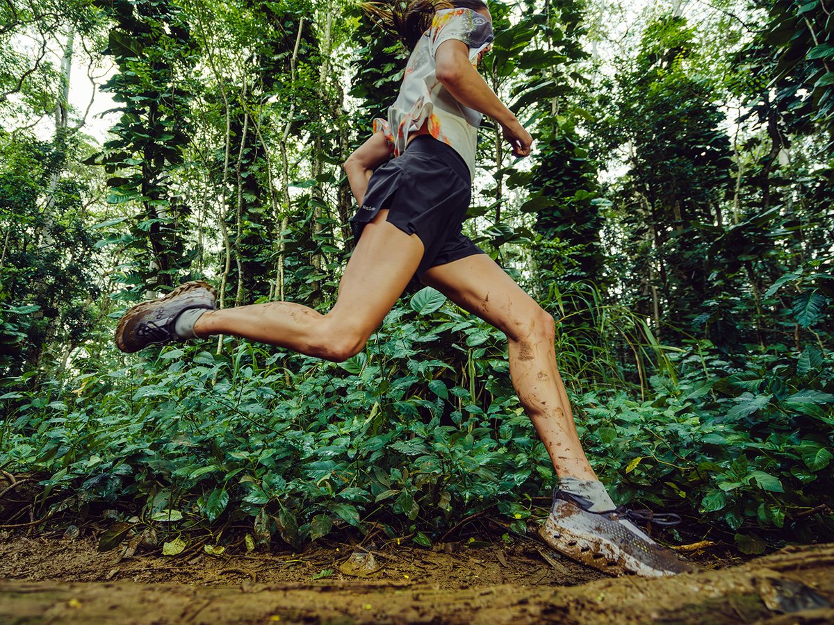 Runner sprinting through a muddy jungle trail.