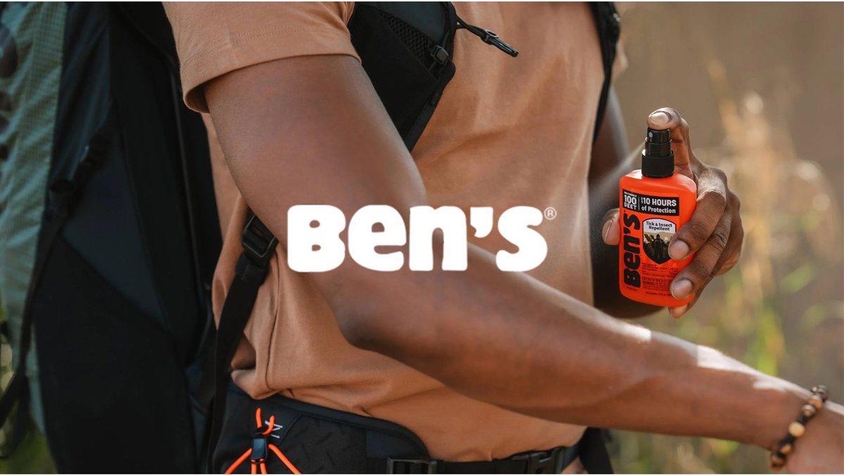 Person holding Ben's 30-hour insect repellent spray bottle while wearing outdoor hiking gear in a natural setting.