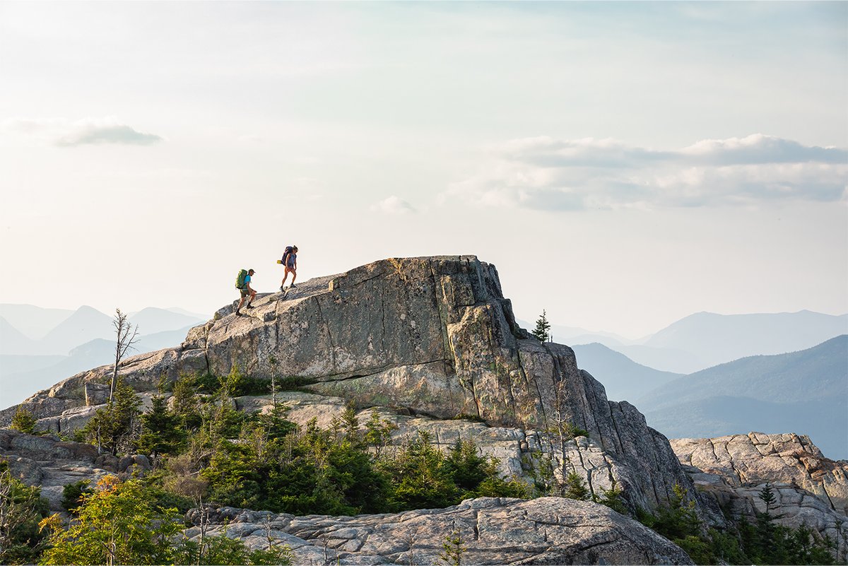 Two backpackers hike up a granite mountain face during a clear day.