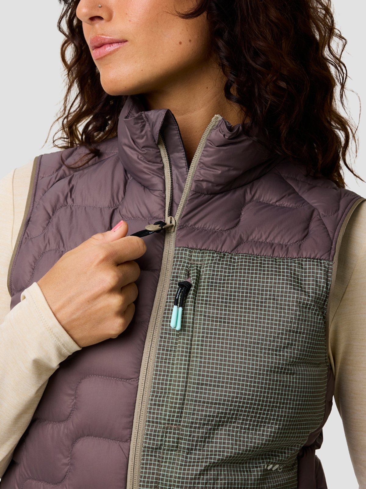 Woman wearing a puffer vest unzips it slightly.