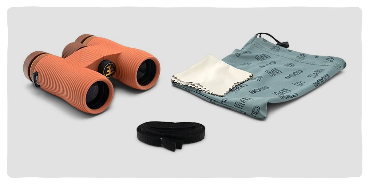 A set of orange binoculars with ribbed grips beside a drawstring carrying case, a lens cleaning cloth, and a removable strap.