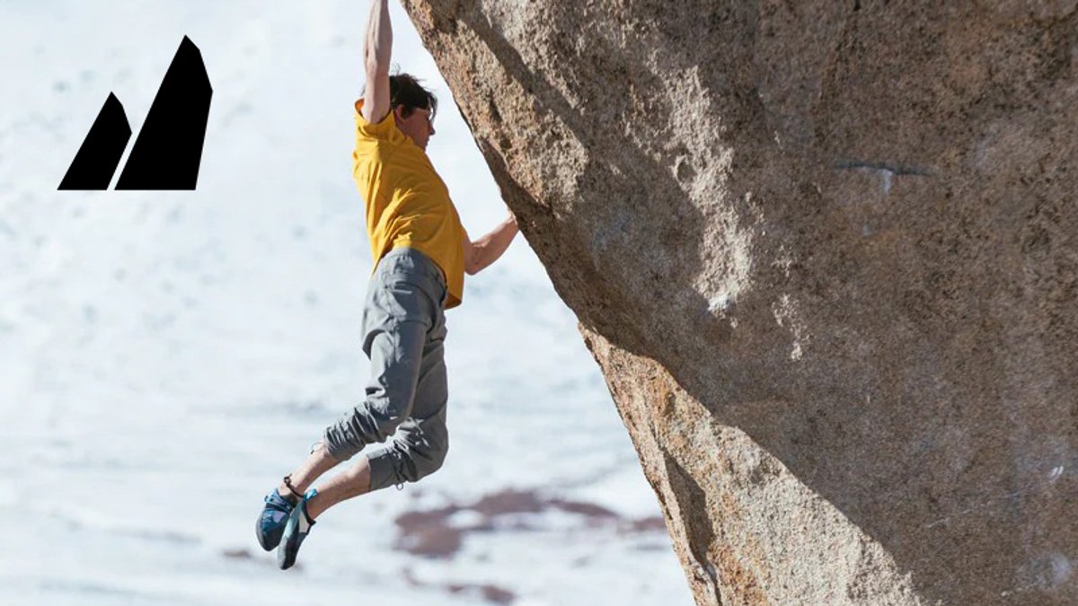 A rock climber in a yellow shirt and blue shoes scales a steep granite boulder face.