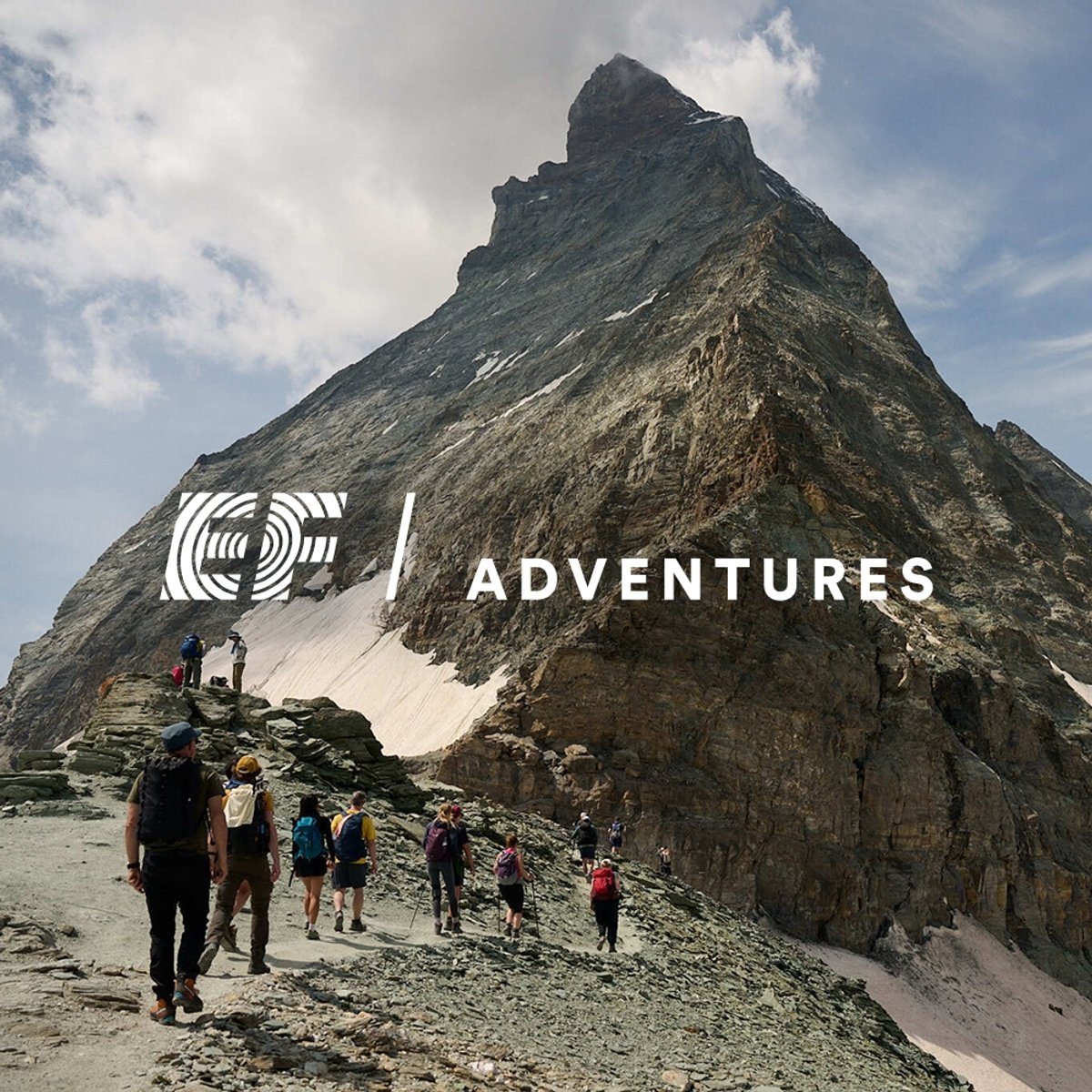 A group of hikers with backpacks and trekking poles traverse a rocky ridge toward the towering Matterhorn under a partly cloudy sky. Featuring the EF Adventures logo overlaid.