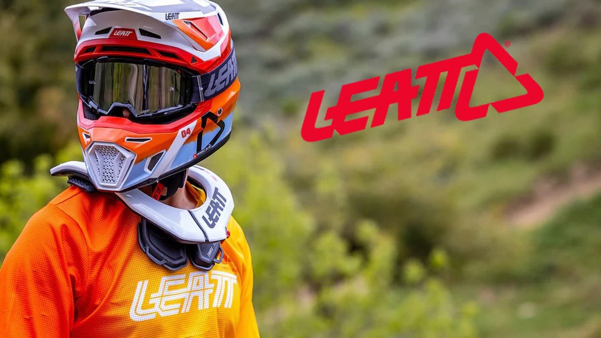 Leatt protective gear featuring a red and white motocross helmet, orange jersey, and white gloves displayed on a rider against a blurred green outdoor background.