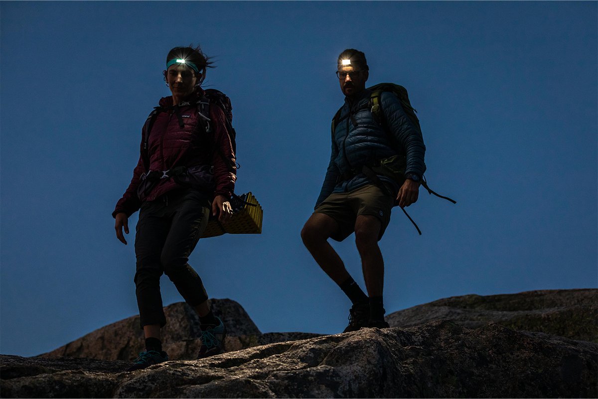 Two hikers wearing headlamps walk down a rocky path.