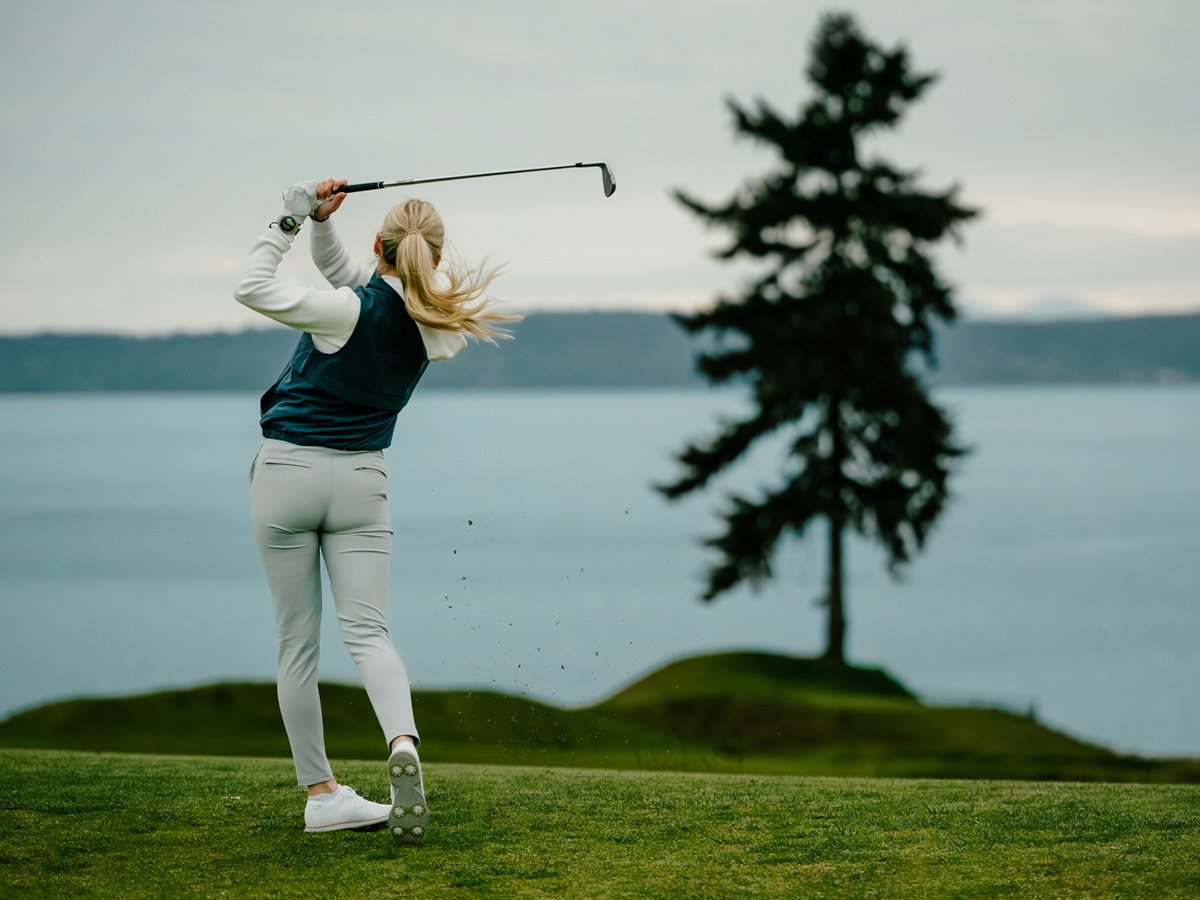 A woman swings her club, dirt flying up in the air.