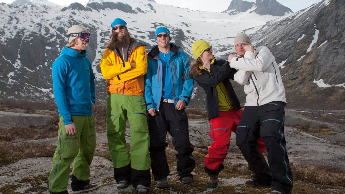 A group of skiiers wearing Norrona Lofoten stand together, laughing in the snowy background.