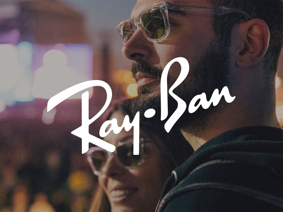 Two people wearing sunglasses on a city street, with the Ray-Ban logo centered over the scene.