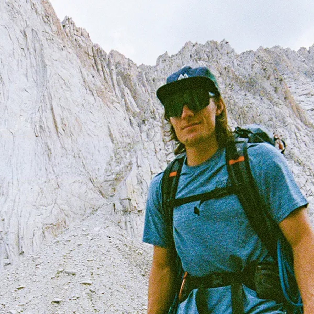 A man stands set against a rocky outcropping, wearing a Mountain Hardwear Sunblocker top.
