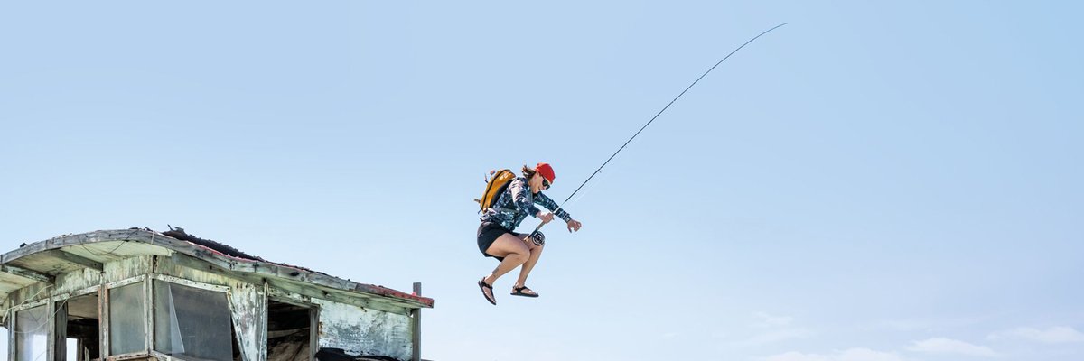 Adventure athlete wakeboarding off a tropical island with a red helmet and backpack while jumping from a weathered wooden pier into crystal blue ocean water.