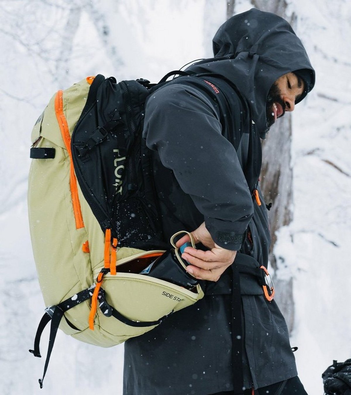 Backcountry skier wearing BCA Float E2 avalanche airbag backpack accessing side storage pocket