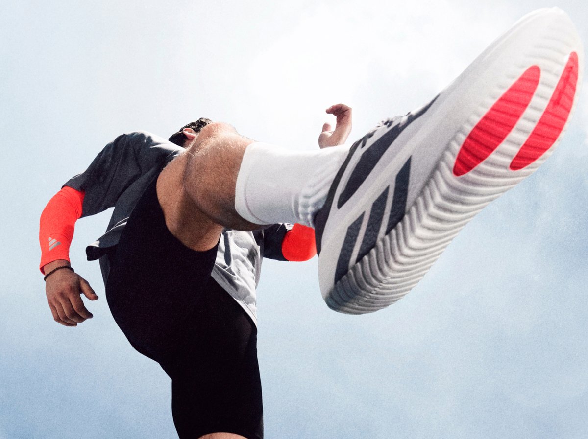 Runner mid-stride in Adidas Hyperboost Edge running shoes shot from a dramatic low angle against an open sky.