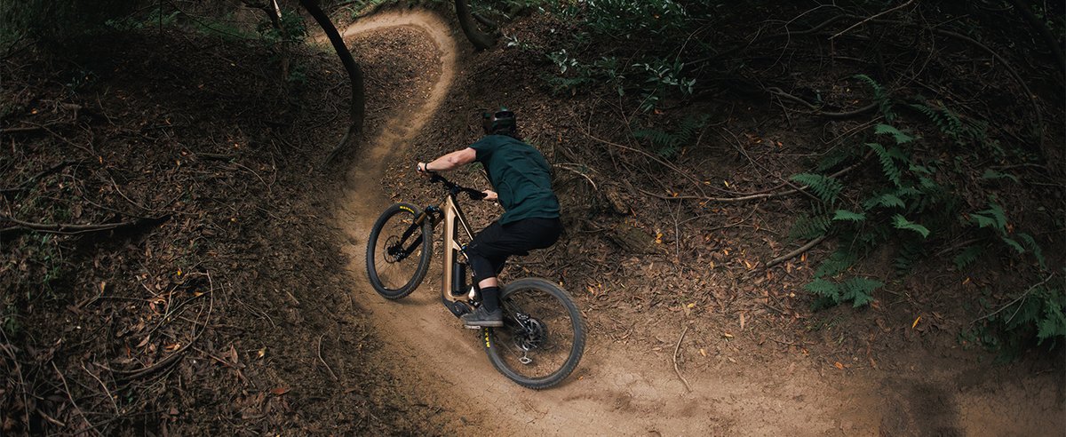 Mountain biker flowing through tight dirt berm turn on wooded forest trail shot from above