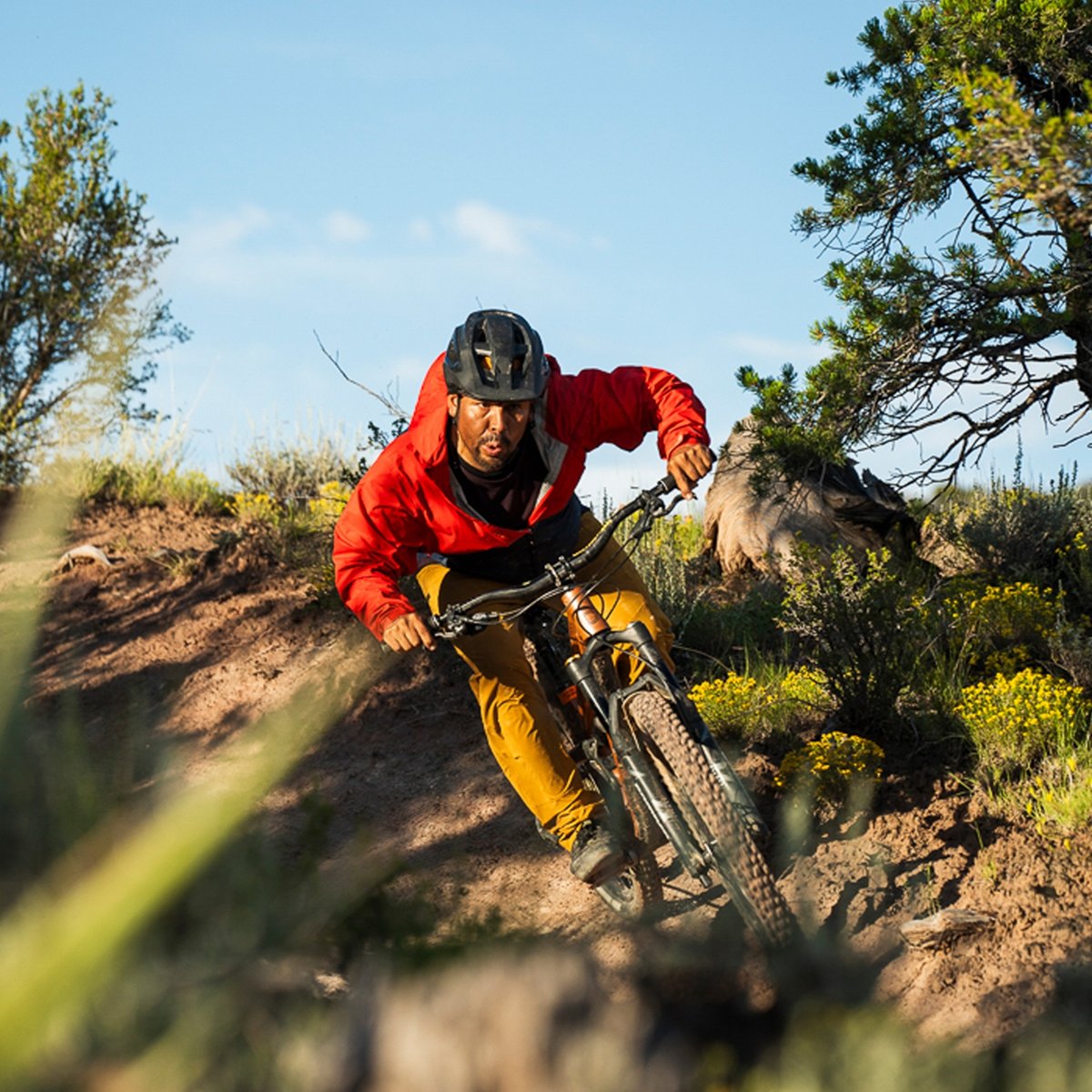 A person in a red jacket and helmet rides a mountain bike around a sharp turn on a dirt trail.