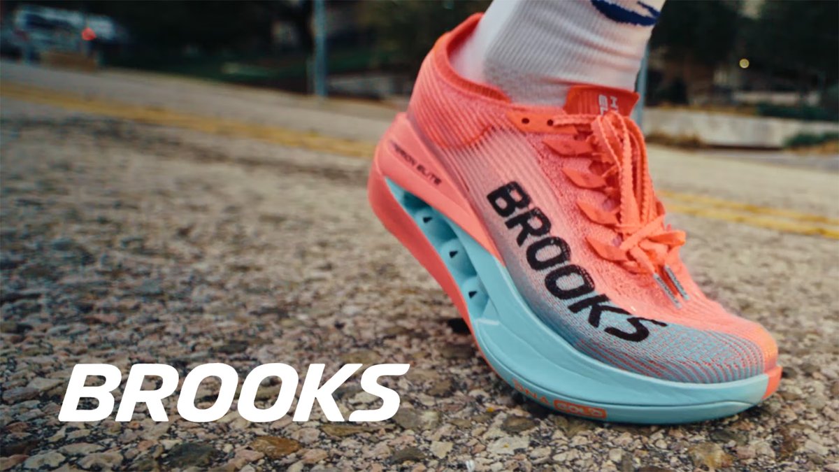 A close-up of a Brooks running shoe in coral and turquoise colors on a concrete surface.