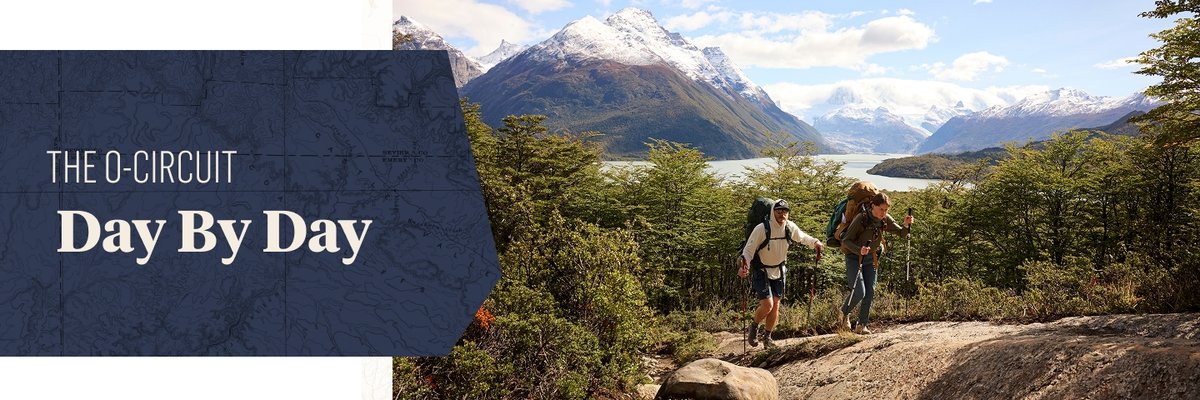 Two hikers wearing bags and using trekking poles crest a rocky path. In the background, towering, snow-covered mountains dominate the sky. The words, “The O-Circuit, Day by Day” appear in a box to the left of the images.