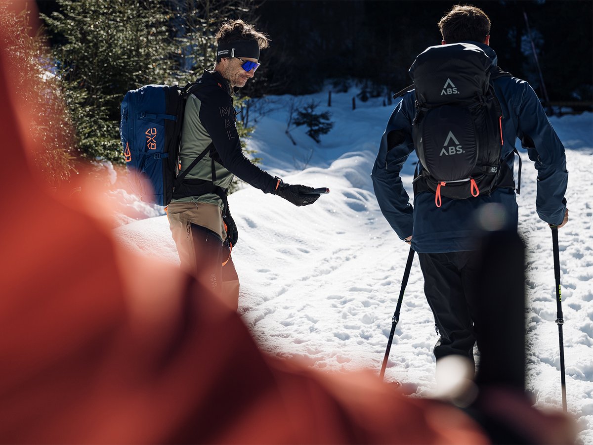 Two ski tourers walking through trees in low winter sun.