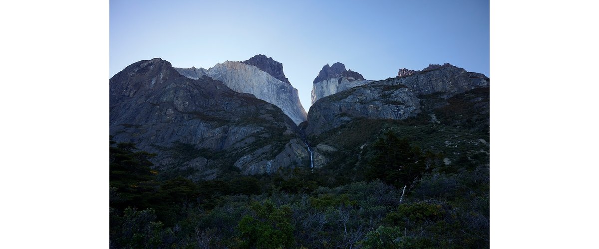 A waterfall pours between two looming mountains.
