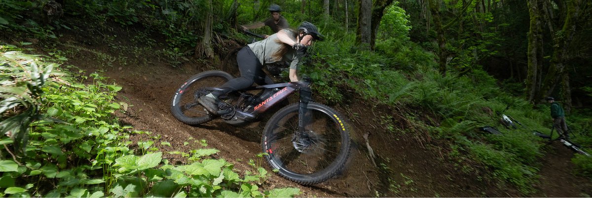 Two e-bike riders on a forested downhill mountain bike trail.
