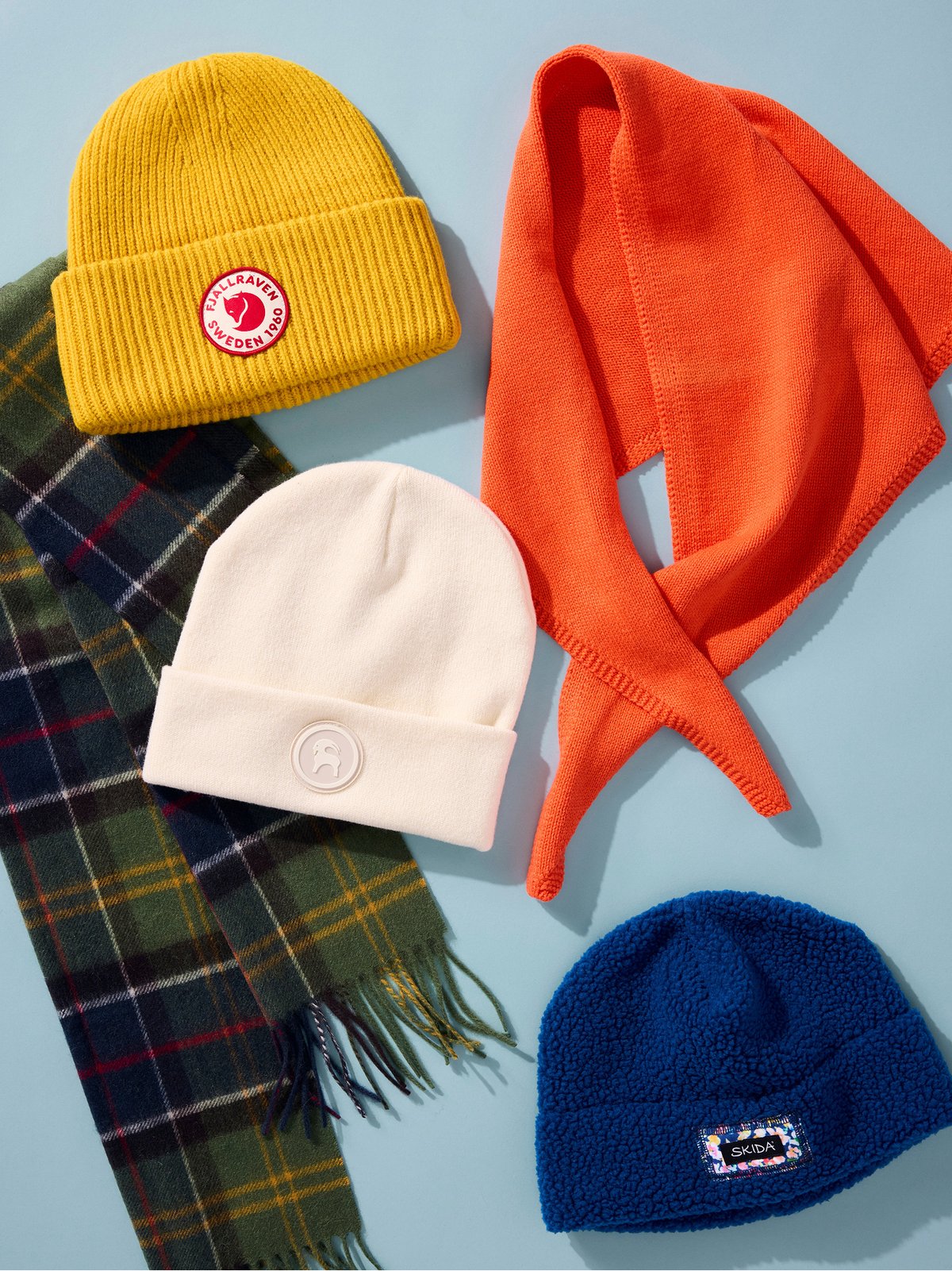 Colorful beanies and scarves arranged on a light blue background.