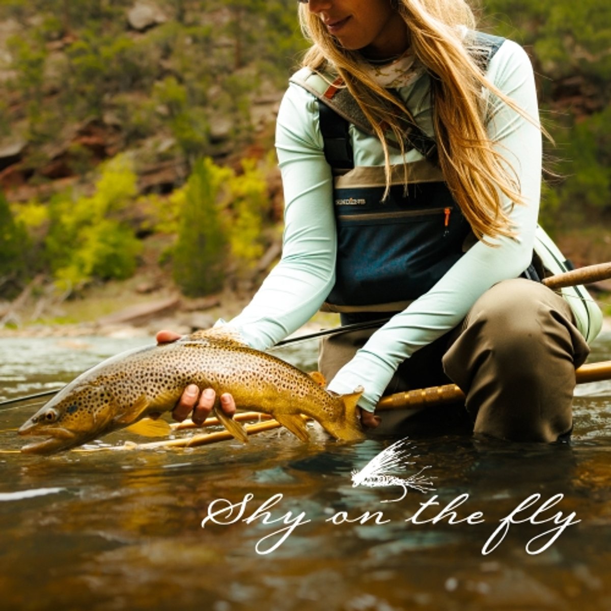 Shyanne Orvis displays a beautiful rainbow trout while kneeling in the river. 