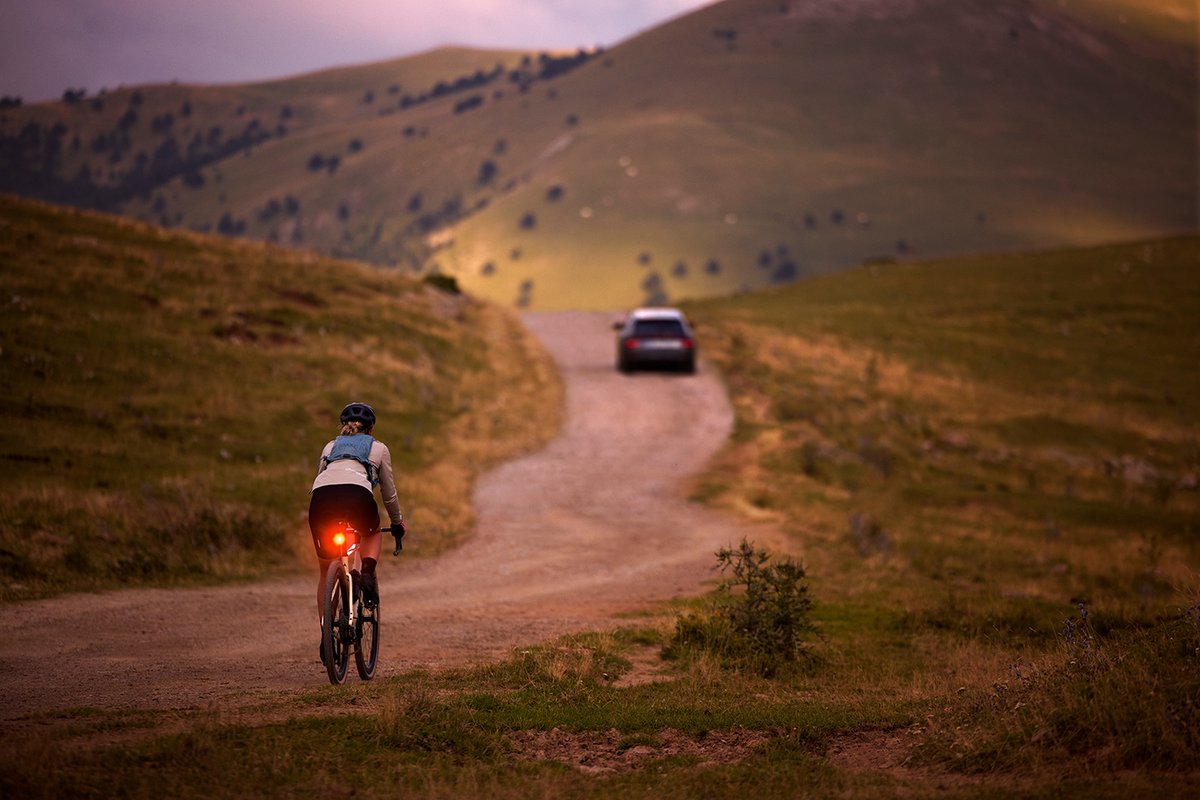 Gravel rider with rear bike light illuminated on open country road at dusk