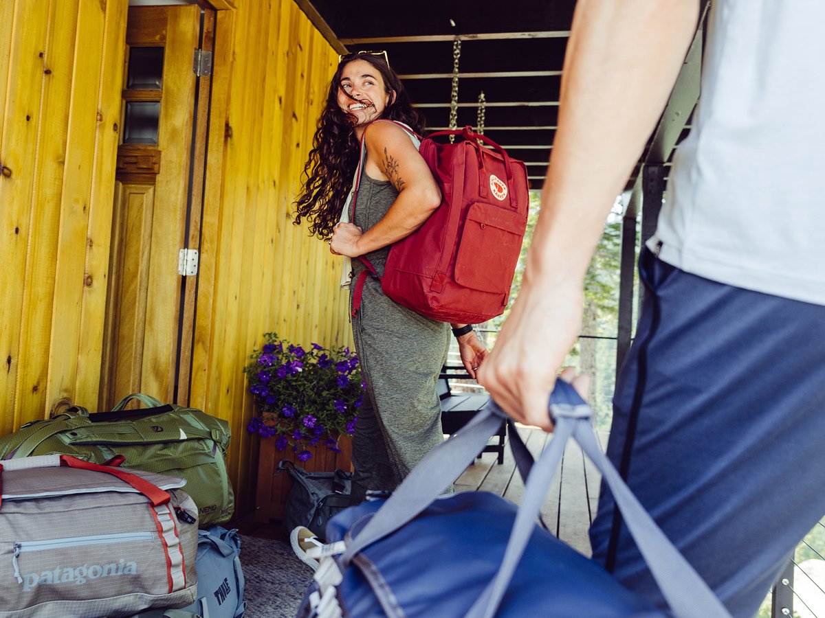 A pair of travelers carrying backpacks and suitcases in a tropical hotel lobby.