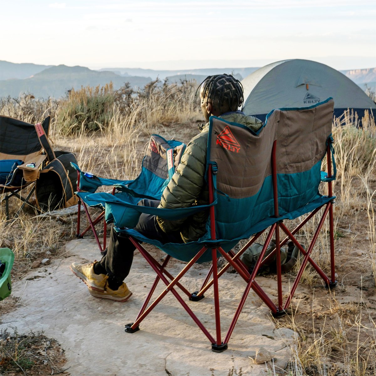 A man reclines in the Kelty loveseat, admiring the view at his campsite.