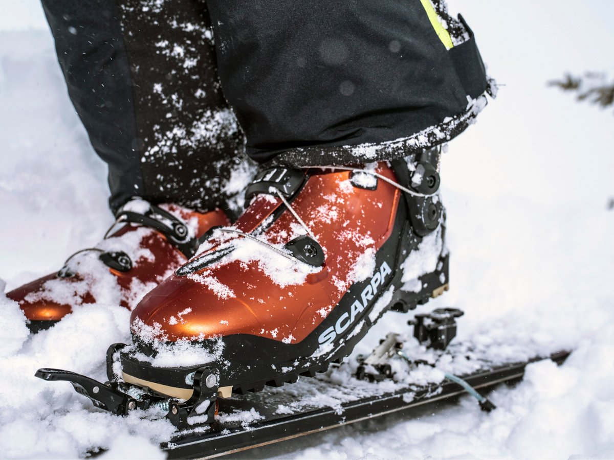 Close-up of the Scarpa F1 ski touring boot clipped into a touring binding, dusted with fresh snow.