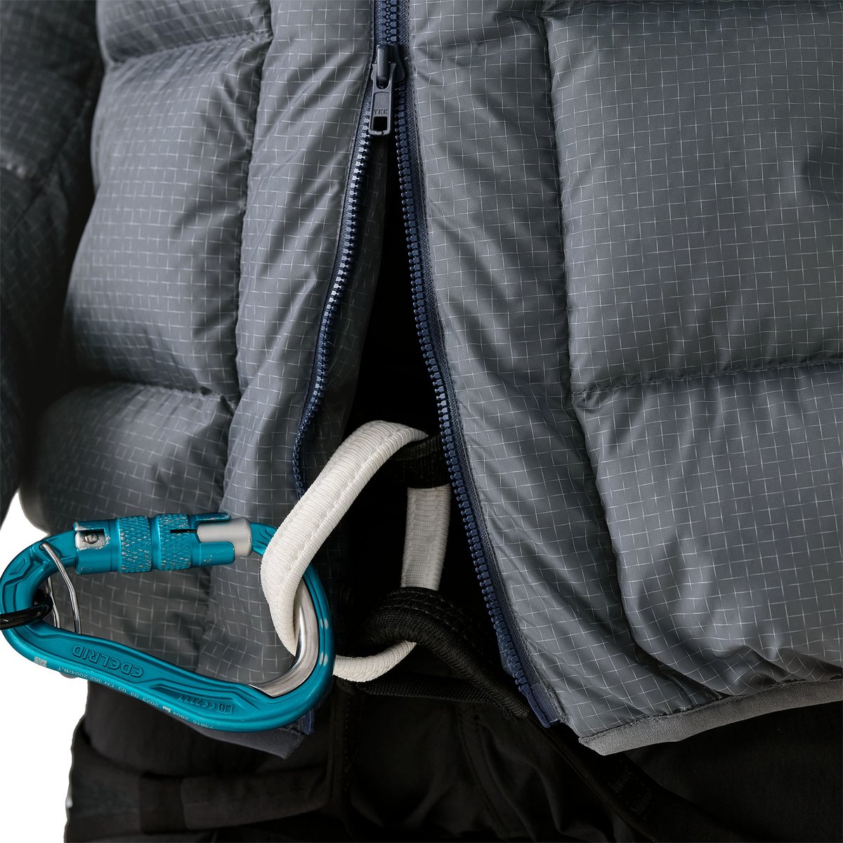 Climber at rest wearing puffy parka laning against rock wall.