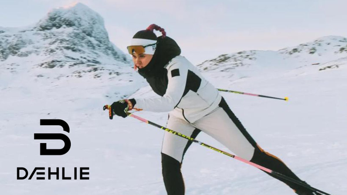 Professional cross-country skier in white and black winter gear racing through snowy mountain terrain with ski poles.