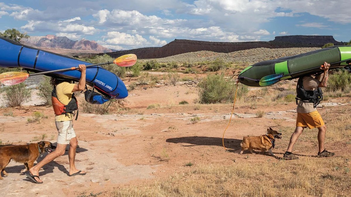 Two men wearing Patagonia Everyday Outdoor items walk while holding rafts above their heads.