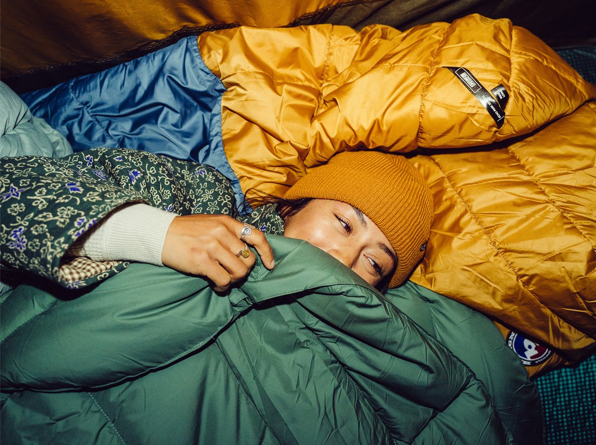 Person bundled in sleeping bags at camp wearing a beanie. Summit+ Club limited time offer.