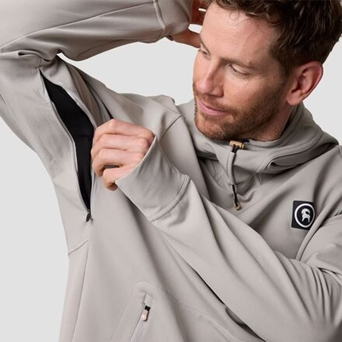 Man wearing a light gray zip-up jacket with black interior lining and branded logo patch, demonstrating the jacket's quality construction and weather-resistant design.