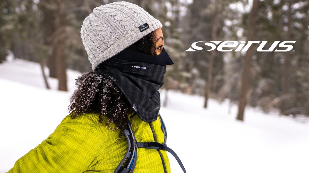 Person wearing a white cable-knit beanie and black Seirus neck gaiter in a snowy forest setting with yellow jacket and backpack.